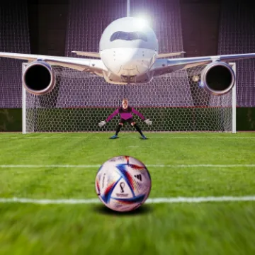 An aircraft parked behind a football goal, with a goalkeeper and a match ball on the grass