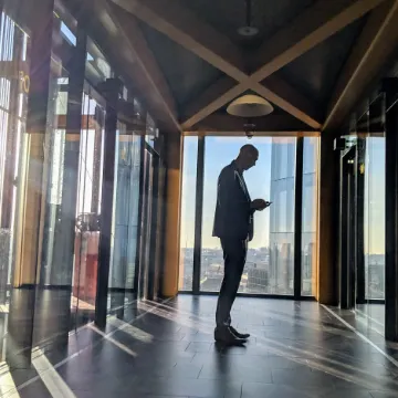 A man at a floor-to-ceiling window in a timber-framed office at sunset
