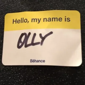 A Behance “Hello, my name is” badge, filled in by hand as “Olly”