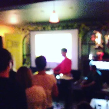 A dim room of people watching a presentation on a projector screen