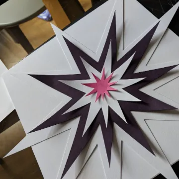 A paper starburst sculpture in white and purple, lying on a table