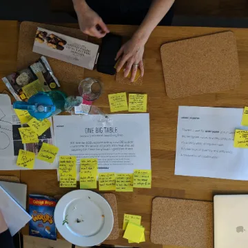 A workshop table covered in worksheets, sticky notes and snacks